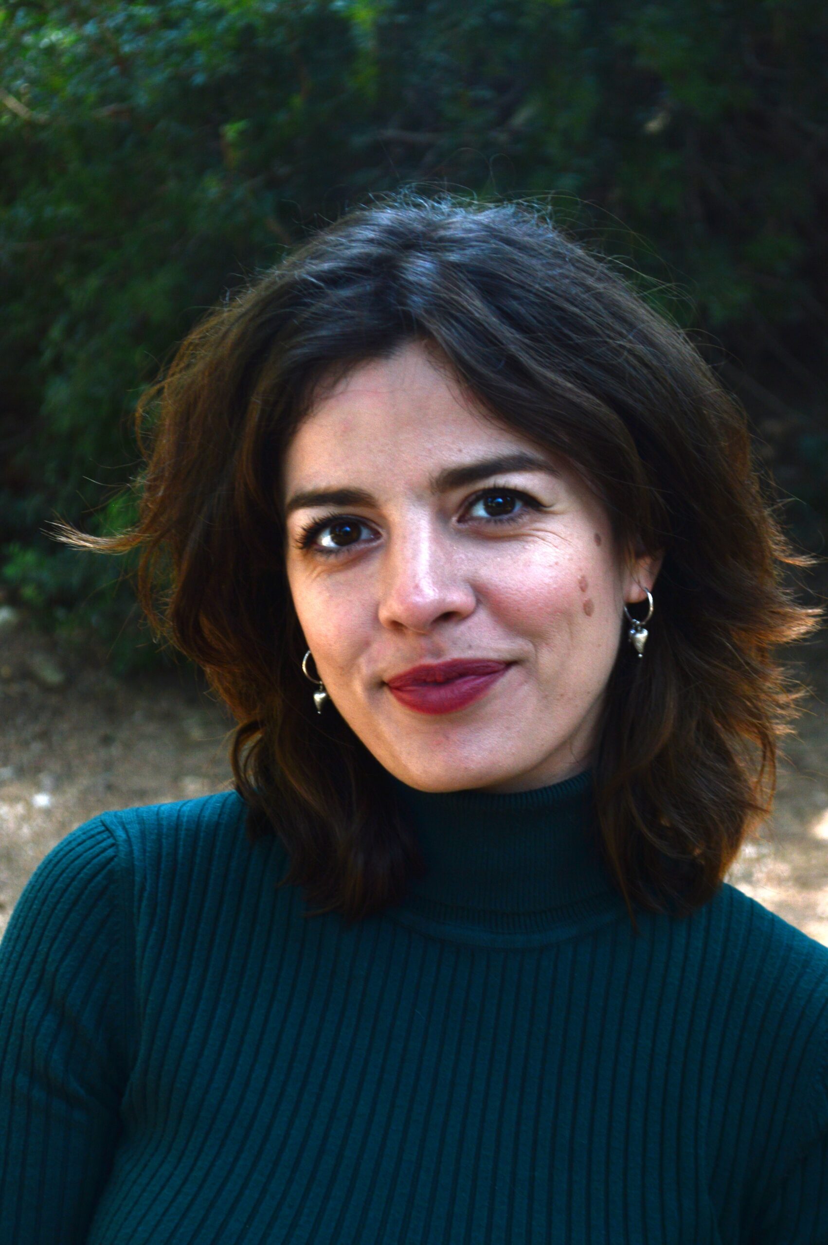 Πορτραίτο της ψυχολόγου που χαμογελά ελαφρά και φοράει κυπαρισσί ζιβάγκο κι ασημένια κρικάκια, με φόντο φύση